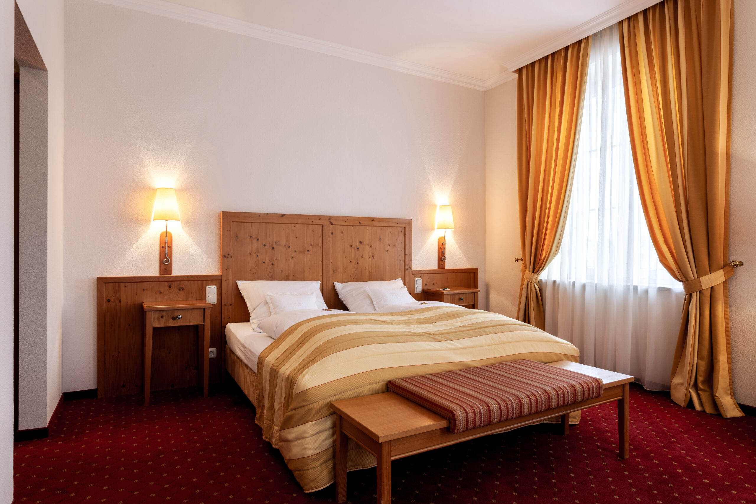 Ein großes Bett in einem unserer Hotelzimmer in Günz. Einladend mit orangenen Vorhängen und rotem Teppich.