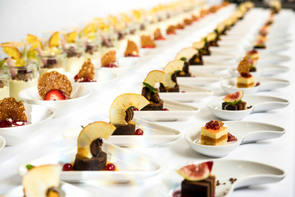 Toll angerichtete Dessertvariationen in einer Reihe auf einer langen Tafel, weiße Schalen runden das Gesamtbild ab.