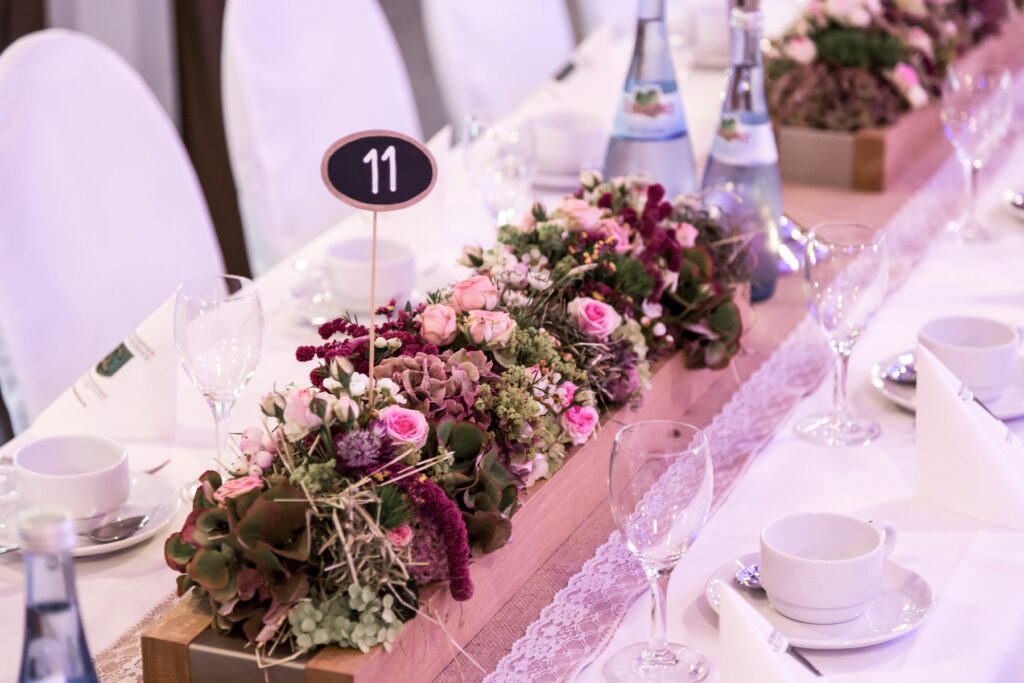 Blumendekoration auf einem Hochzeitstisch, inklusive Tischnummer und einer fertig eingedeckten Tafel.