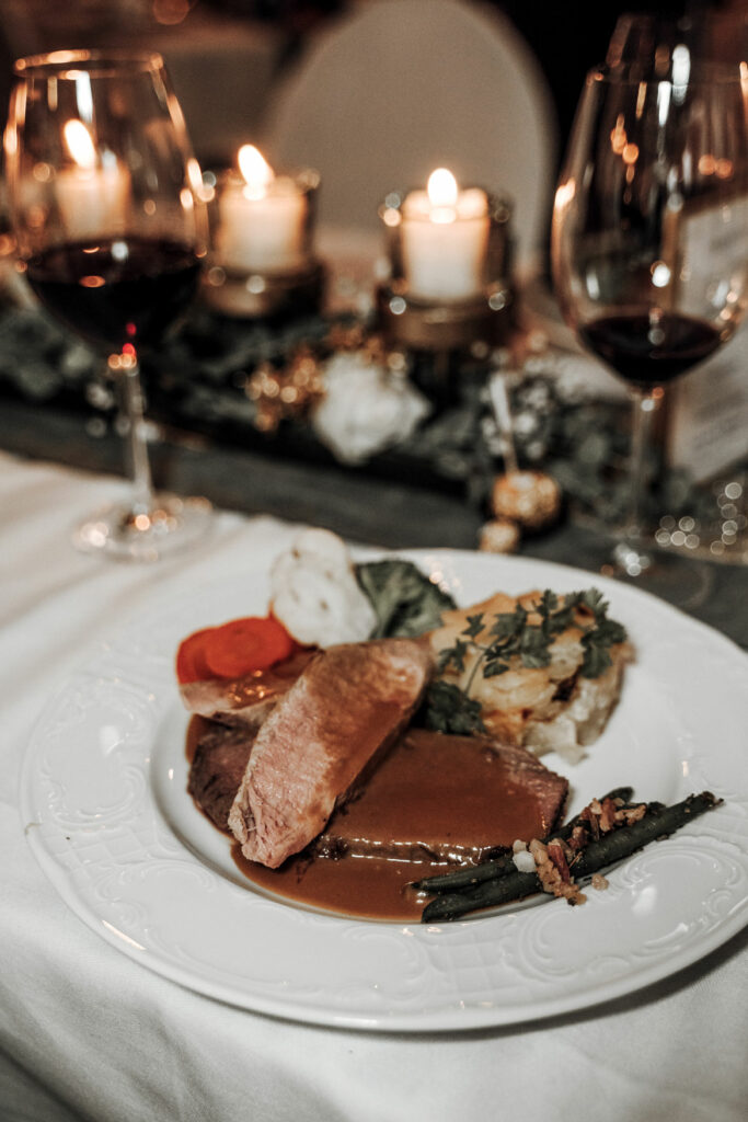 Eine toll angerichtete Hauptspeise auf einem weißen Teller mit Rotweingläsern im Hintergrund.