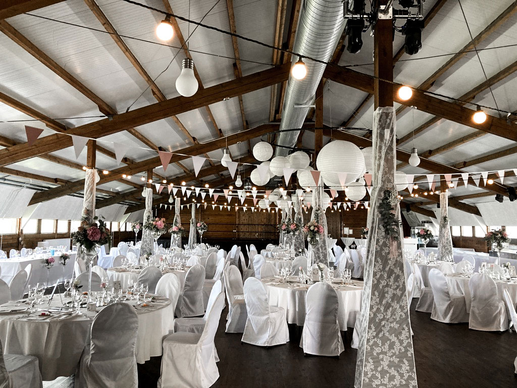 Ein Rundumblick auf den in weiß dekorierten Feststadl in Günz, Girlanden an der Decke, weiße, elegante Hussen über den Stühlen.