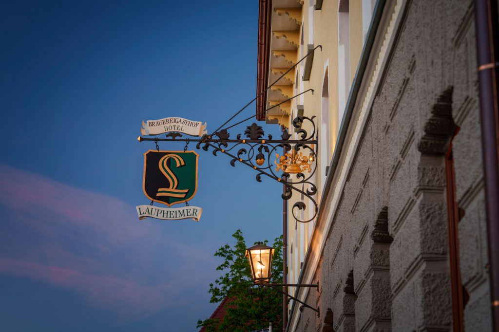Außenansicht des Brauereigasthof-Hotels Laupheimer in Günz im Allgäu mit traditionellem Wirtshausschild – stilvolles Ambiente am Abend.